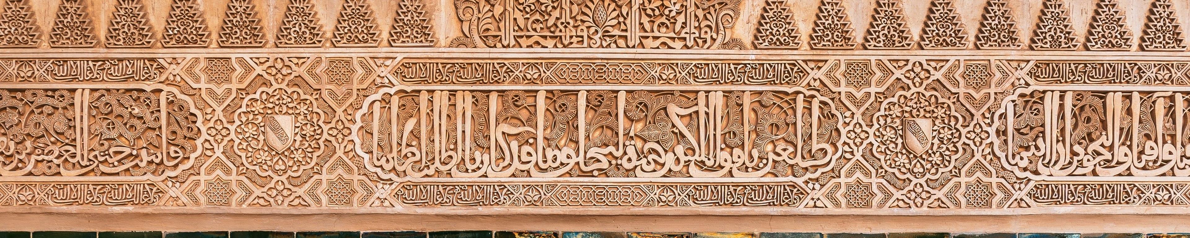 A carved plaster frieze in the Alhambra: a band of Arabic inscription in deep relief, framed by roundels and a run of finer interlaced ornament.