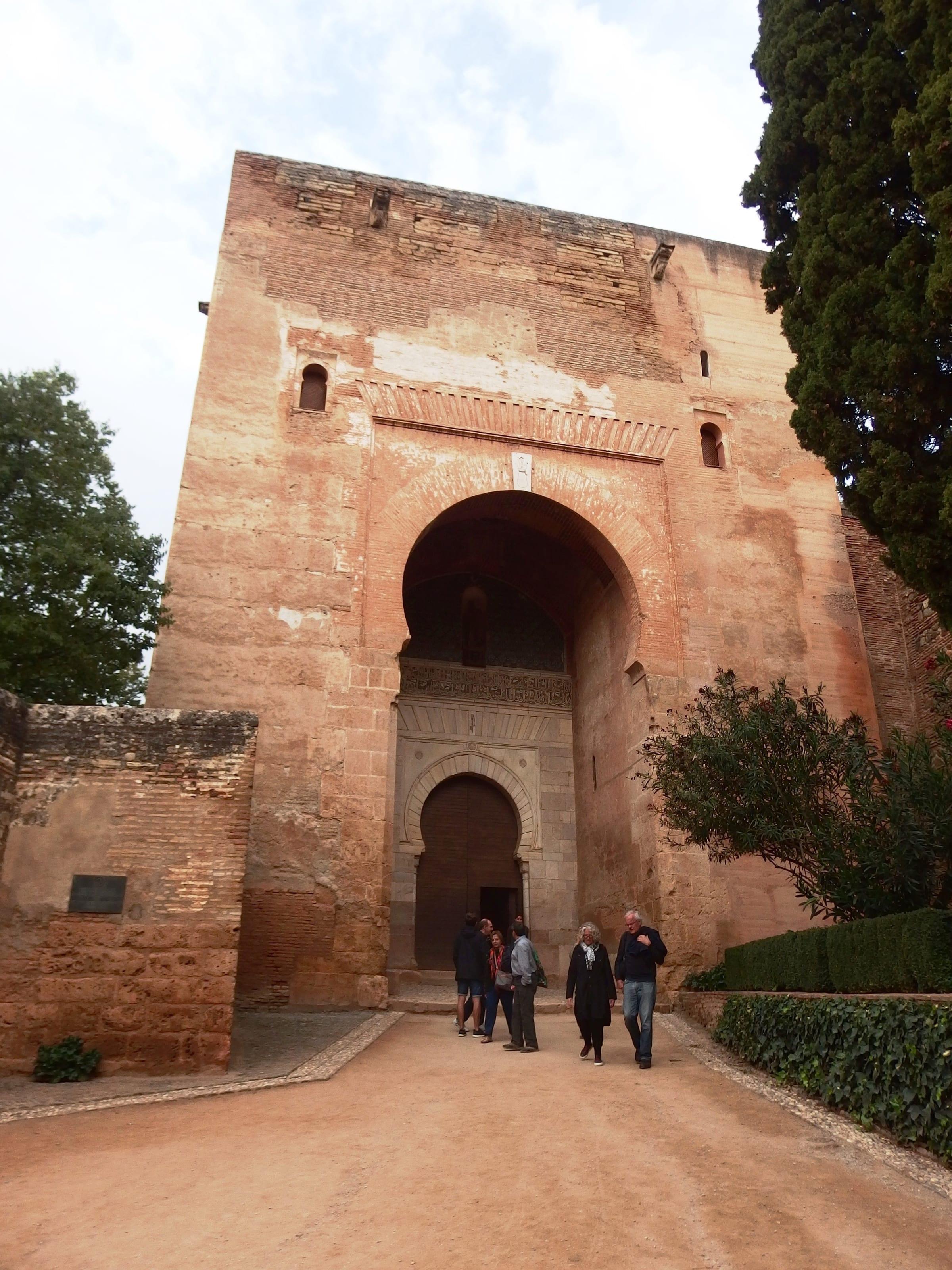 The Puerta de la Justicia, the great horseshoe-arched gate into the Alhambra, with a small group of visitors walking through it.